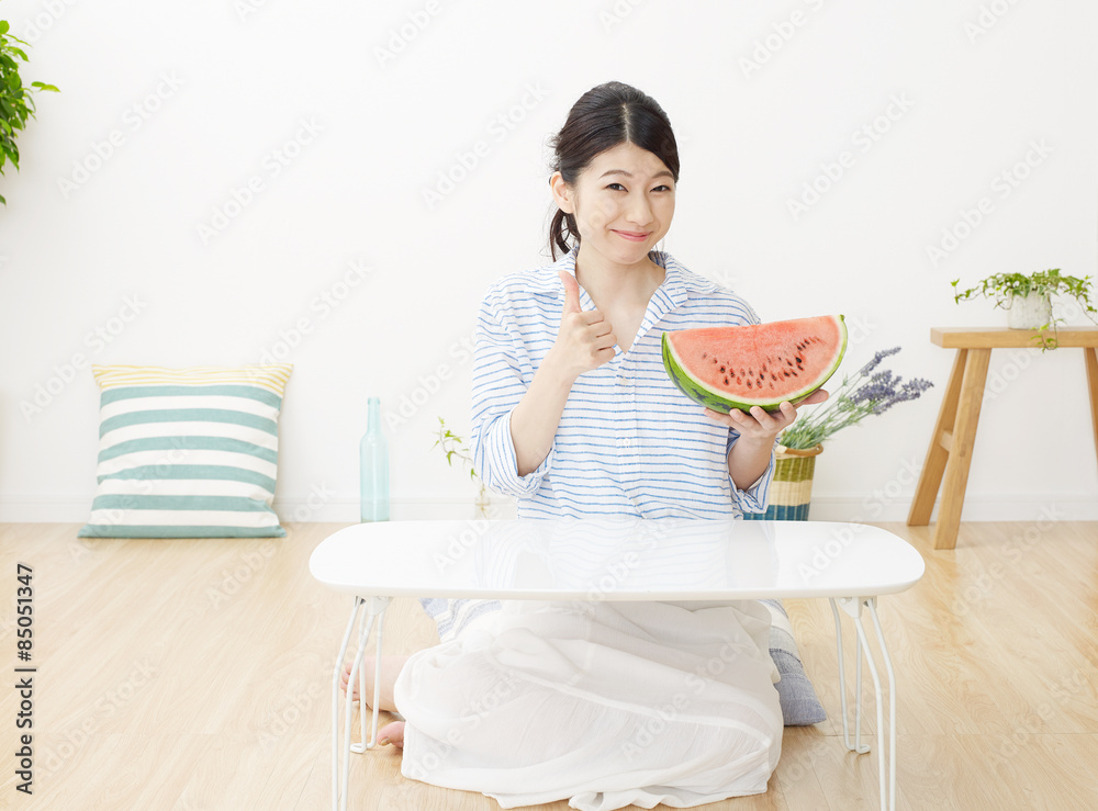 部屋で西瓜を食べる女性　グッドサイン