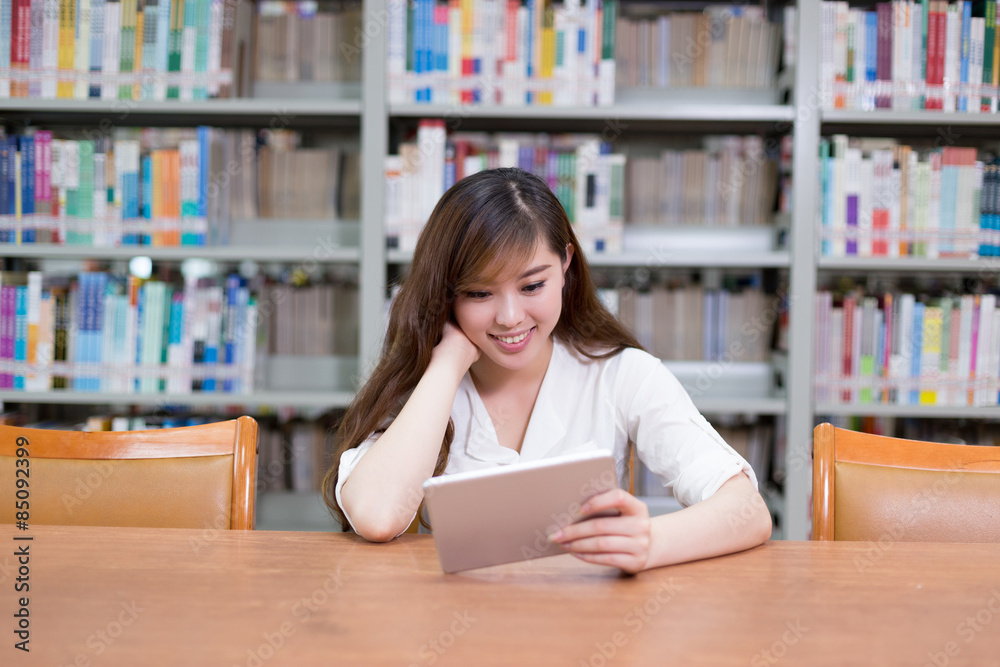 漂亮的亚洲女学生在图书馆使用数字平板电脑