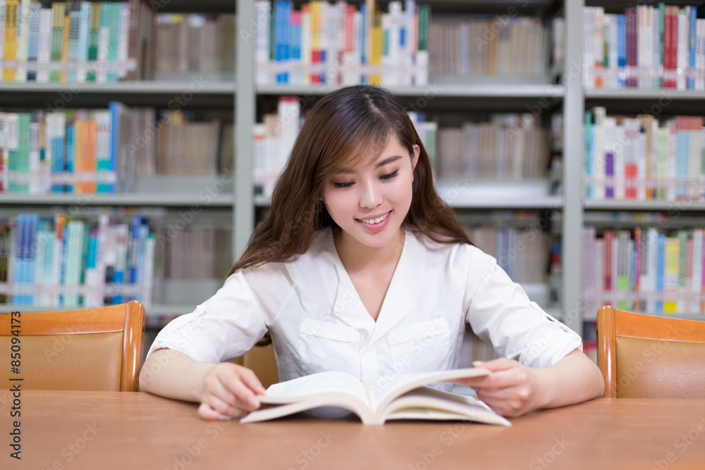 漂亮的亚洲女学生在图书馆看书