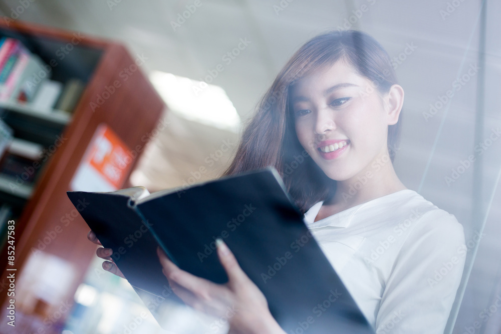 beautiful asian female student reading book in library