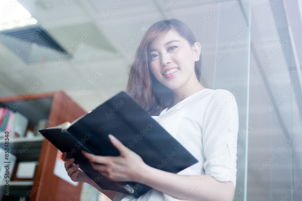 美丽的亚洲女学生在图书馆看书