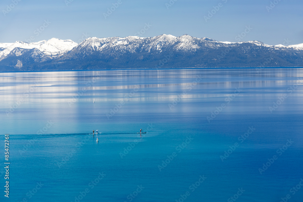 三名男子划着桨登上平静的太浩湖，可以看到内华达山脉的雪峰。