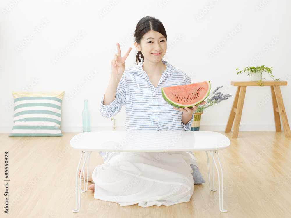 部屋で西瓜を食べる女性　ピースサイン