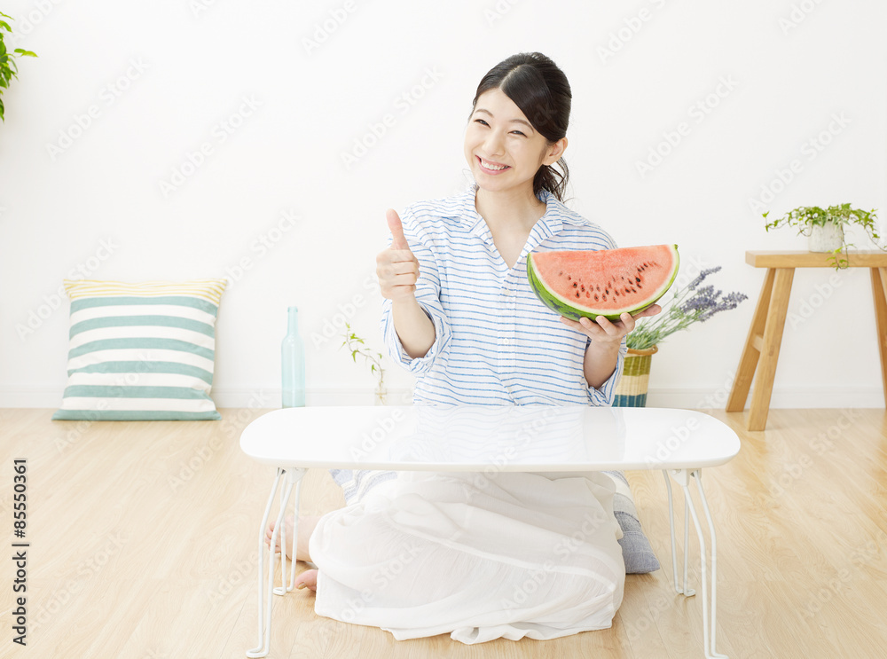 部屋で西瓜を食べる女性　グッドサイン