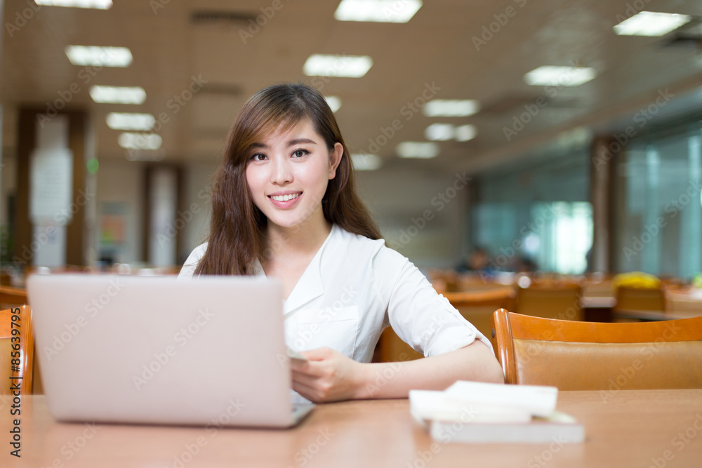 亚洲美女女学生在图书馆用笔记本电脑学习