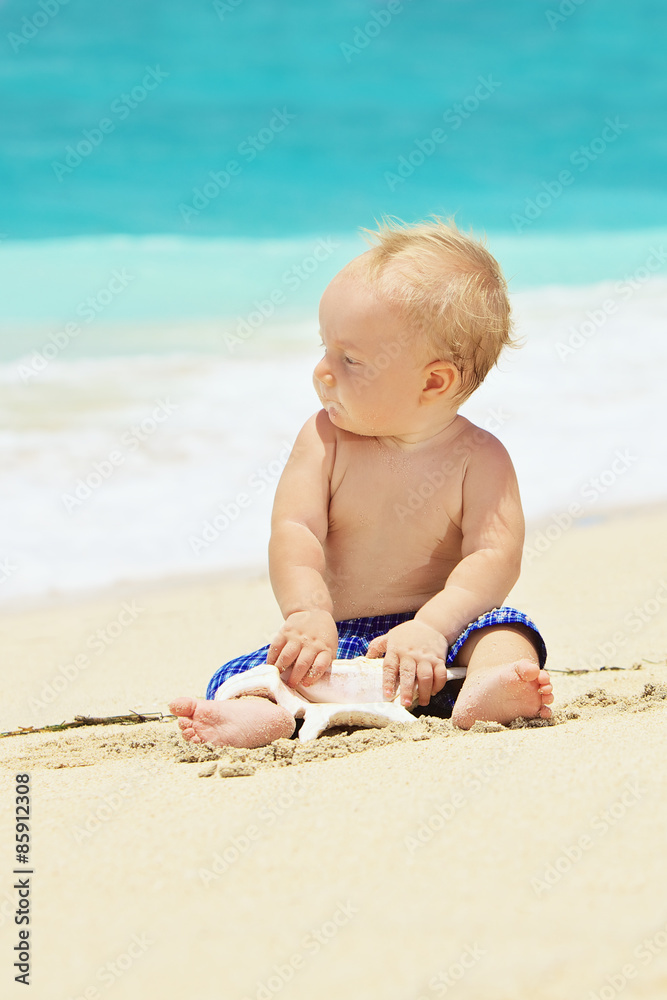 Portrait of child sitting and playing alone with sea shell with fun on balinese sand ocean beach bef