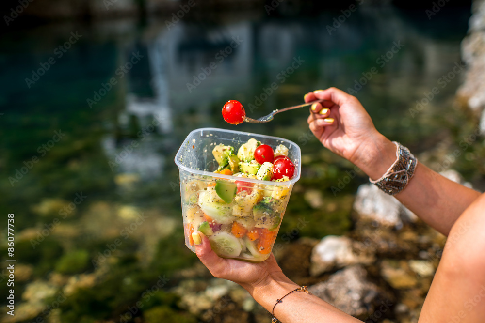 Woman eating healthy salad near the river