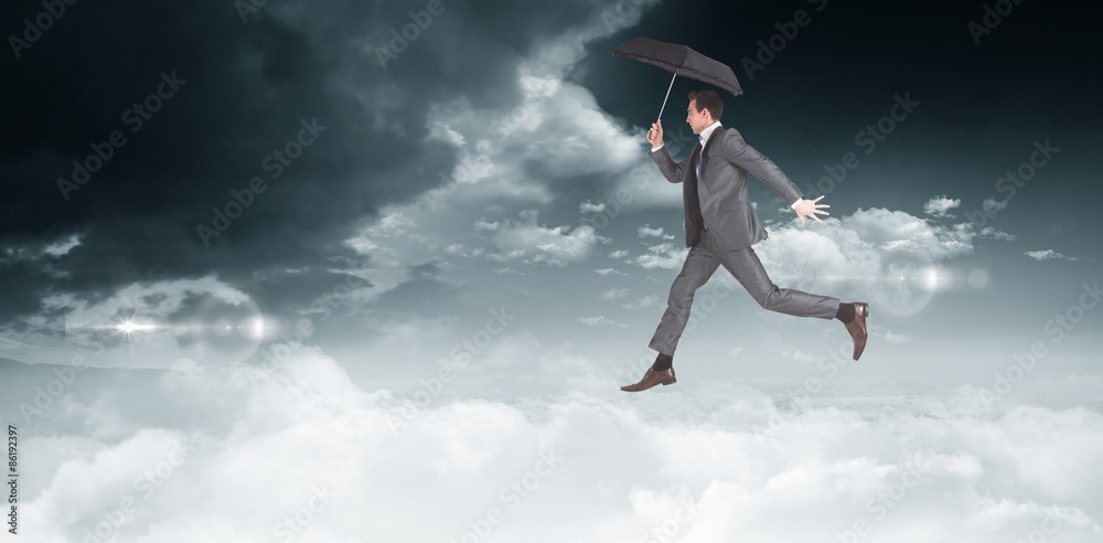 Composite image of businessman jumping holding an umbrella