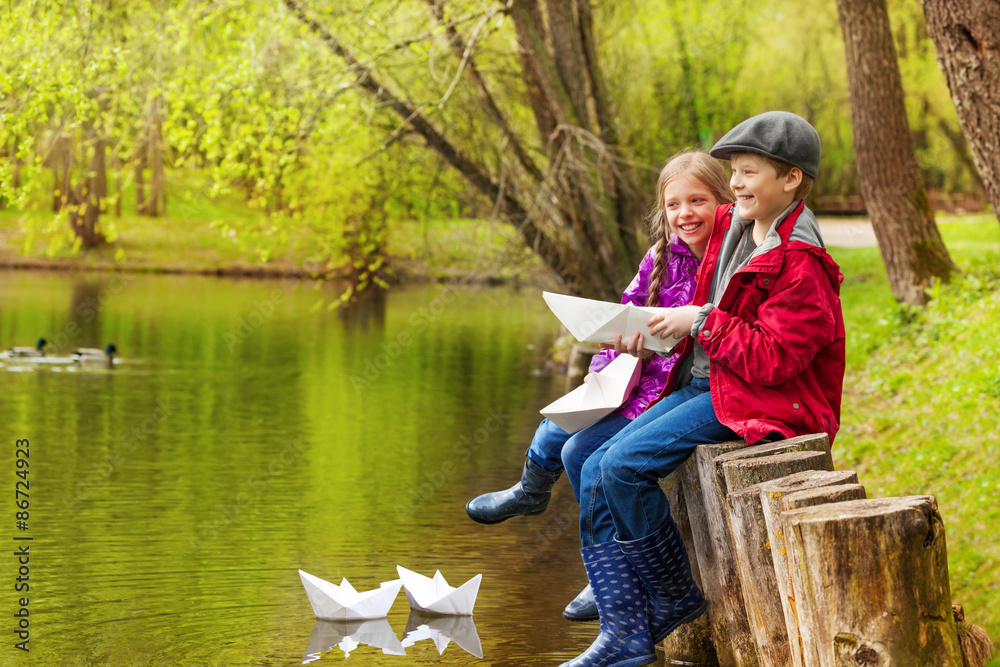 Laughing girl and boy near pond with paper boats