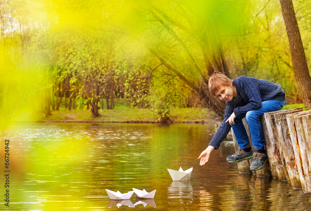 Boy holding arm to play with white paper boats