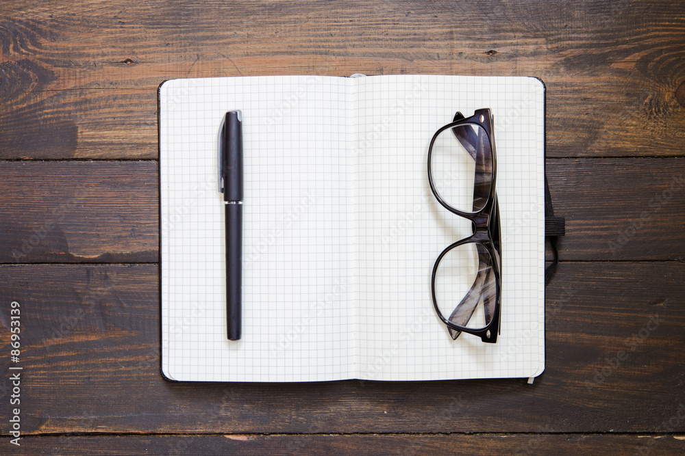 Reading glasses and notepad on wooden background