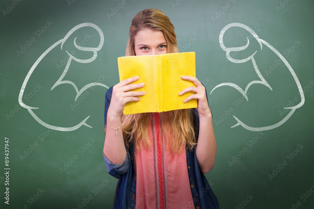 Composite image of student covering face with book in library 