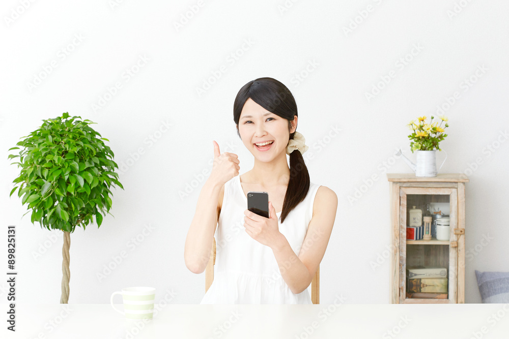 部屋でスマートフォンを持ってグッドサインする女性