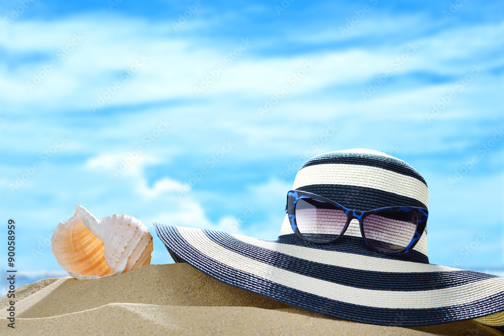 Summer hat and sun glasses and seashell on the sandy beach in summer with blue sea and sky travel ic