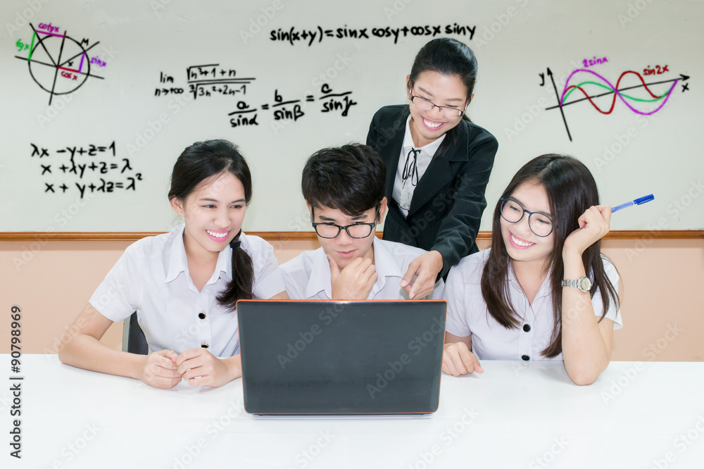 Asian teacher assisting student using laptop at desk in classroo