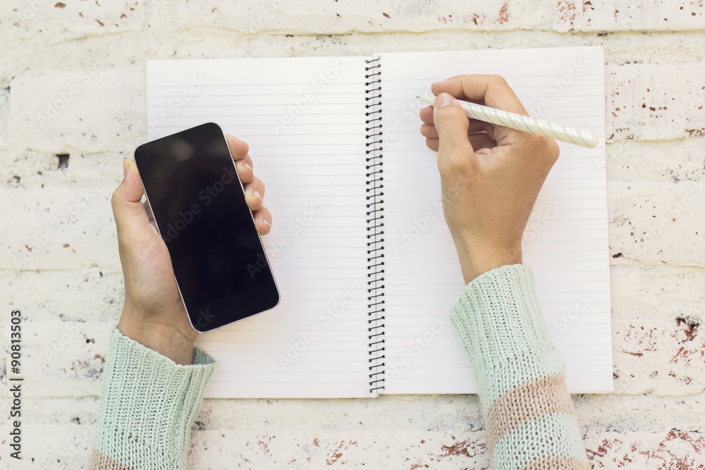 Girl hands with smartphone and blank diary with pen on a wooden