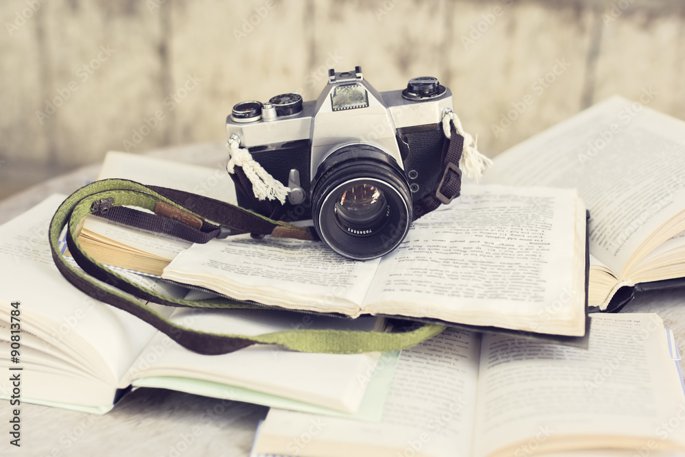 Old camera and many open books on a wooden table