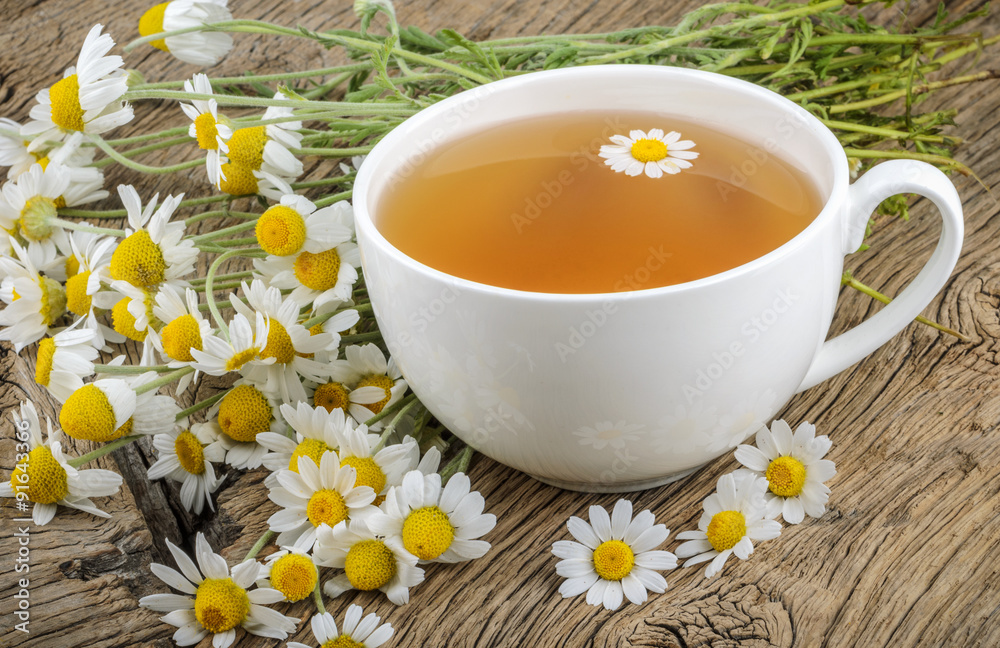 Cup of tea and chamomiles on wooden background