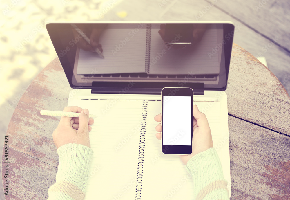 girl writing in a notebook with a cell phone and a laptop, vinta