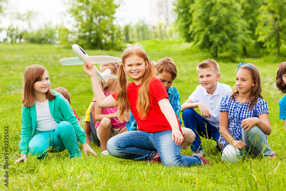 Girl holds airplane toy and children sit behind