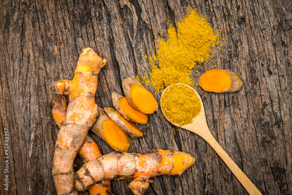 turmeric powder in spoon and roots on wooden plate