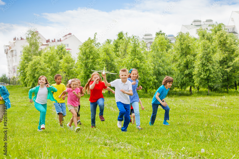 Running boy with airplane toy and children behind