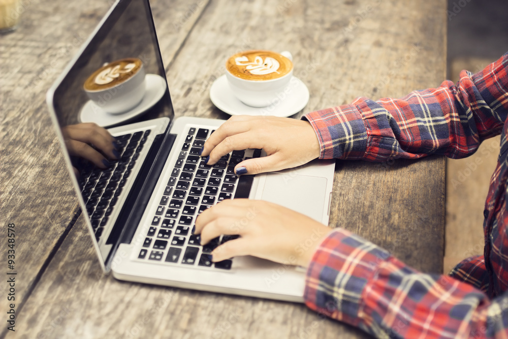 Hipster girl with laptop and cup of coffee ona wooden table