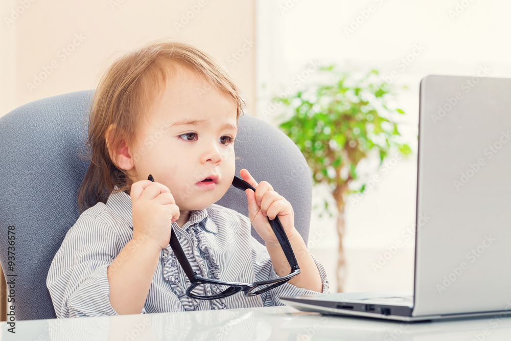 Toddler girl putting on big glasses while using her laptop