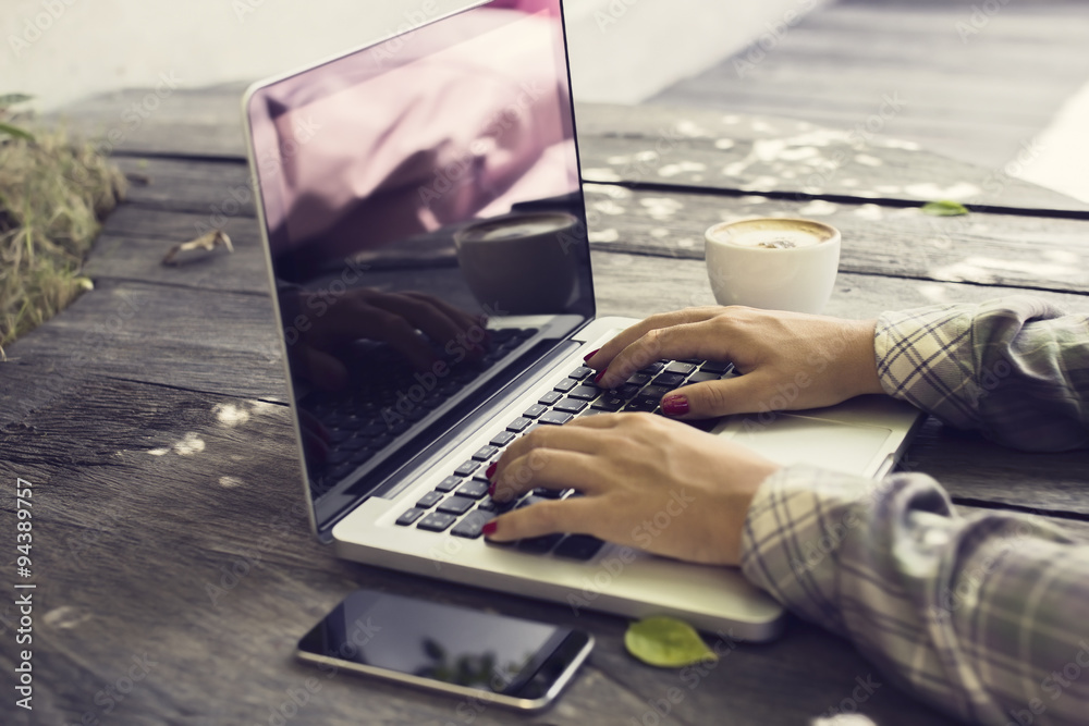 Schoolgirl typing on a laptop, with cell phone and coffee outdoo