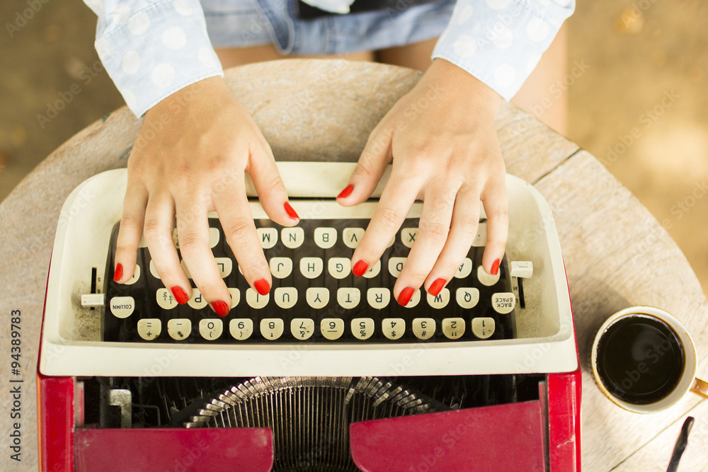 Girl typing on the old typewriter with a cup of coffee outdoors