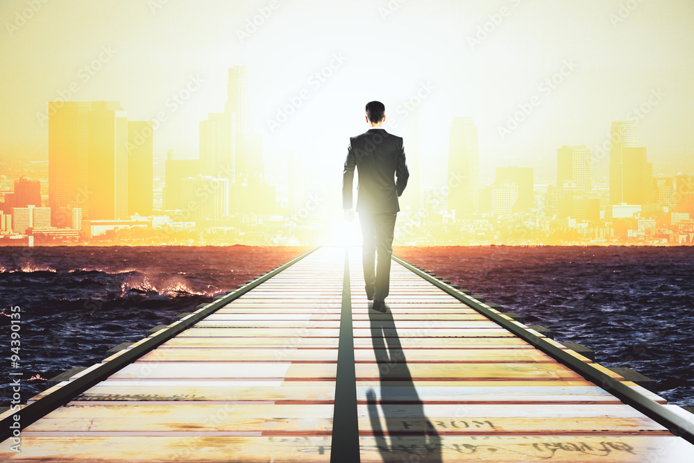 Businessman walking on a straight road to the big city at sunris