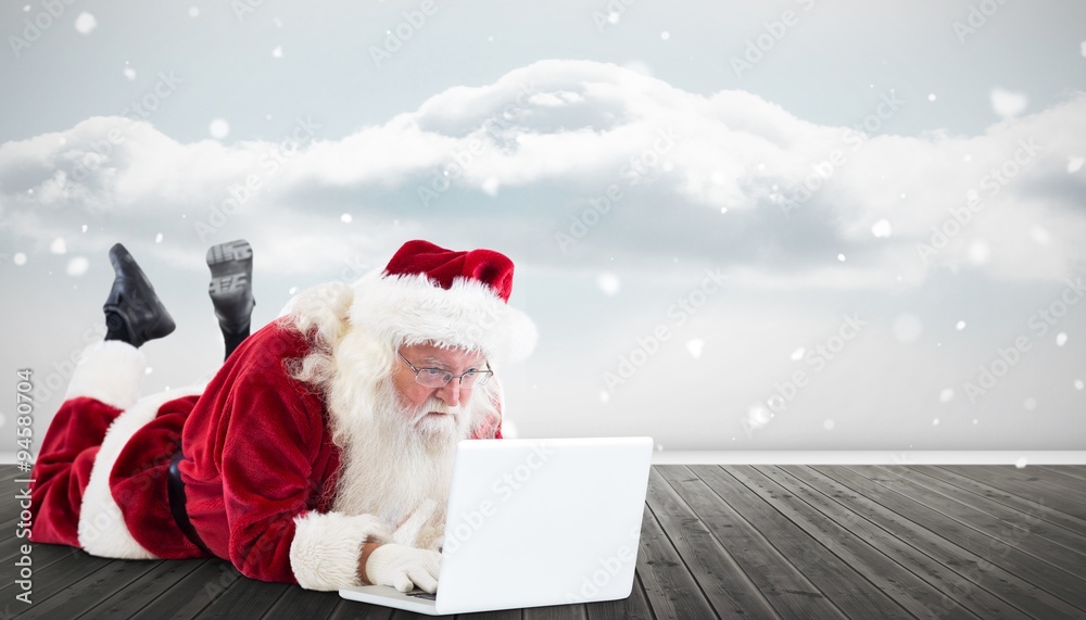 Composite image of santa lies in front of his laptop