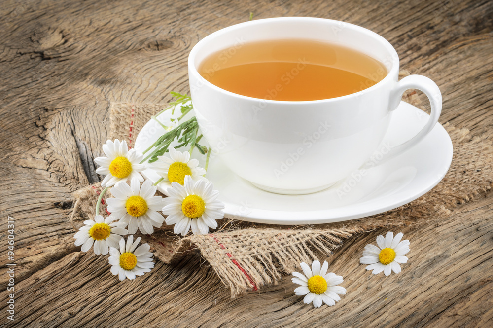 Cup of tea and chamomiles on wooden background