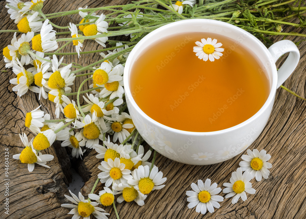 Cup of tea and chamomiles on wooden background