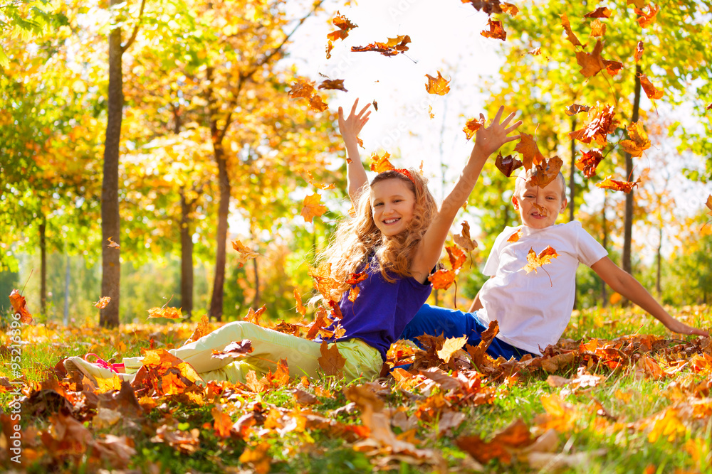 Happy boy and girl play with leaves in forest