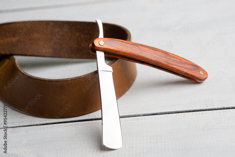 Stragth razor  and leather belt on wooden background