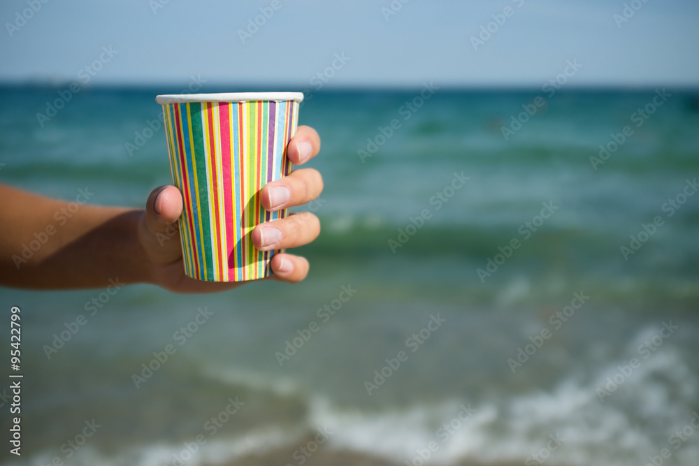 Paper cup with coffee in hand on the sea background