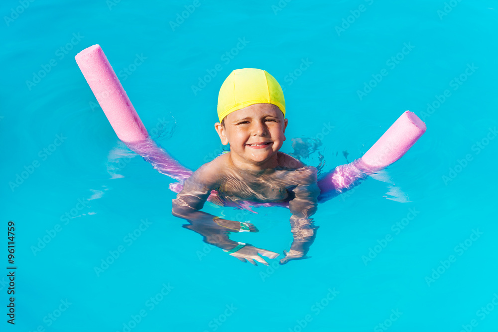 Smiling boy learns how to swim with pool noodle