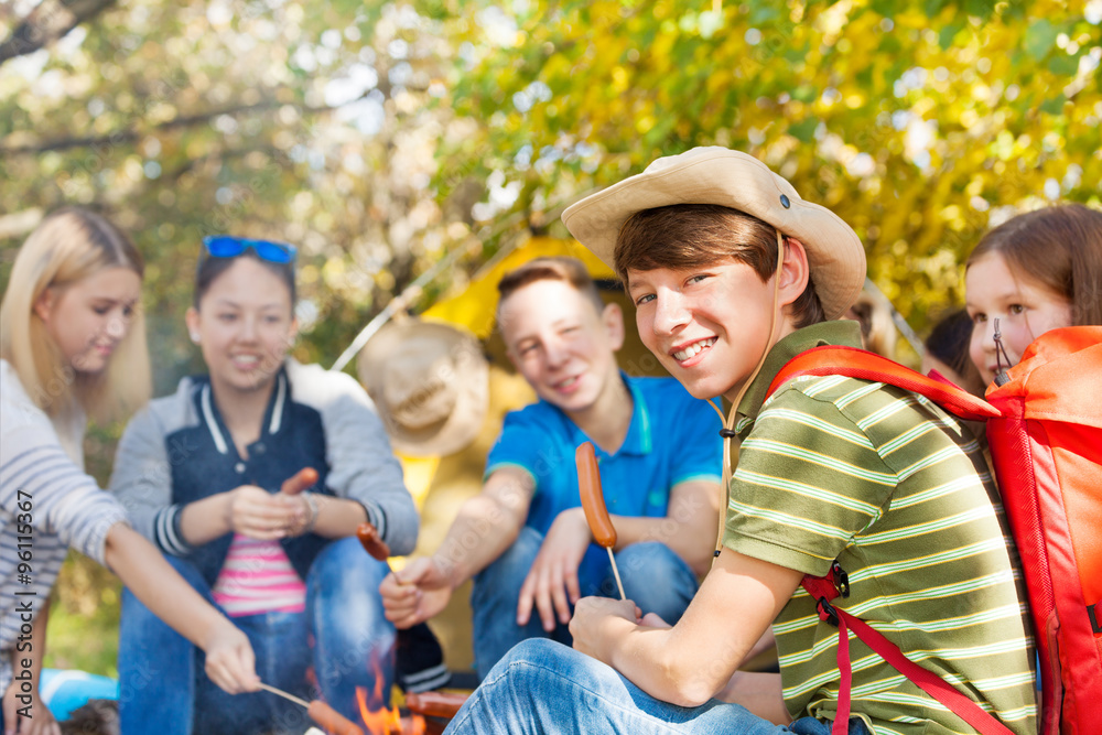 Friends on campsite with sausages sticks in forest