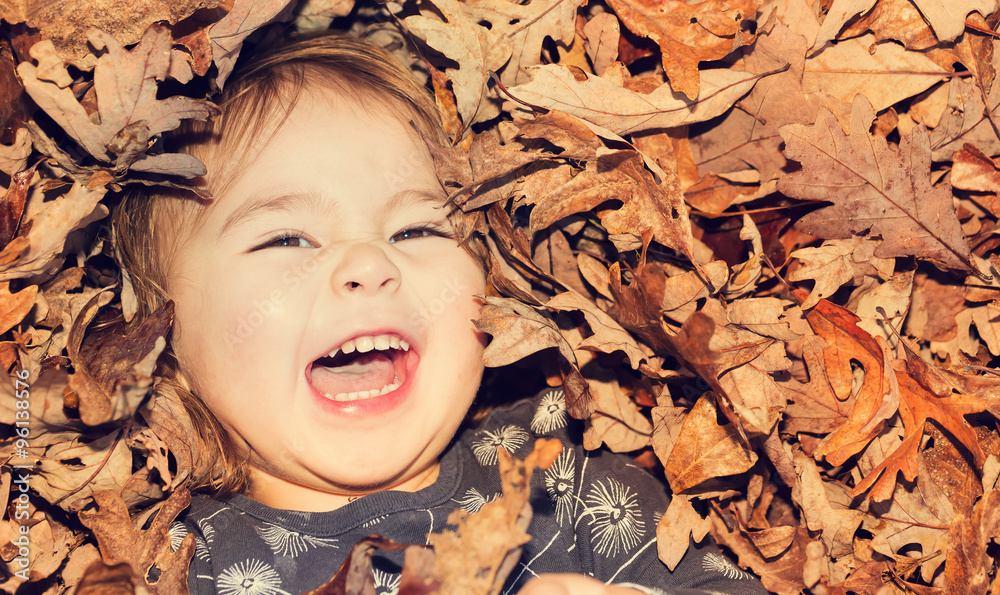 Happy toddler girl smiling while lying down in a pile of leaves