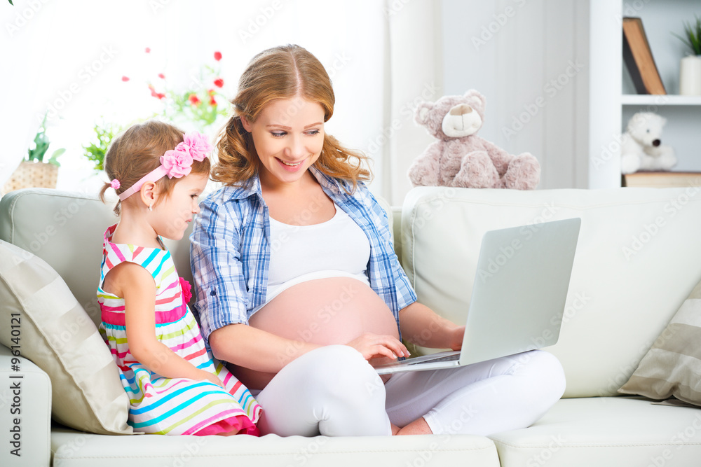 Happy family pregnant woman and child with a laptop at home