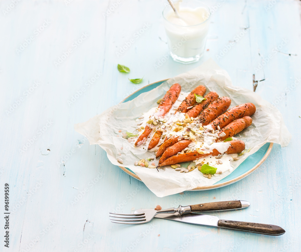 Roasted young carrots with cream and seeds in ceramic plate over blue wooden background