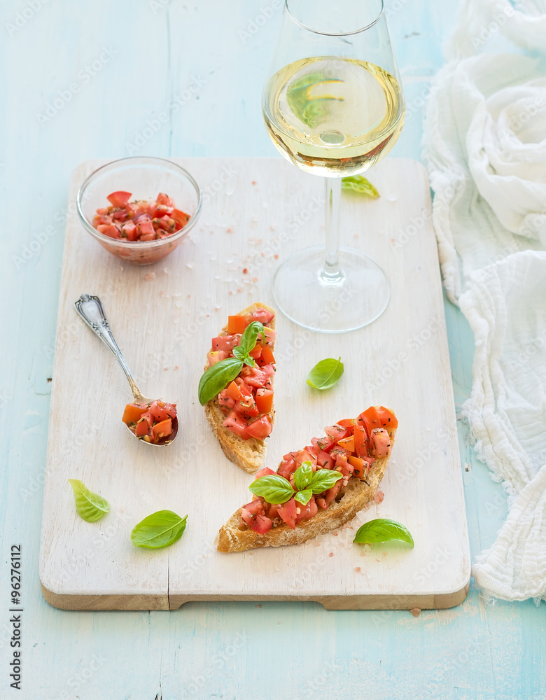 Tomato and basil bruschetta sandwich on white wooden serving board over rustic blue background, top 