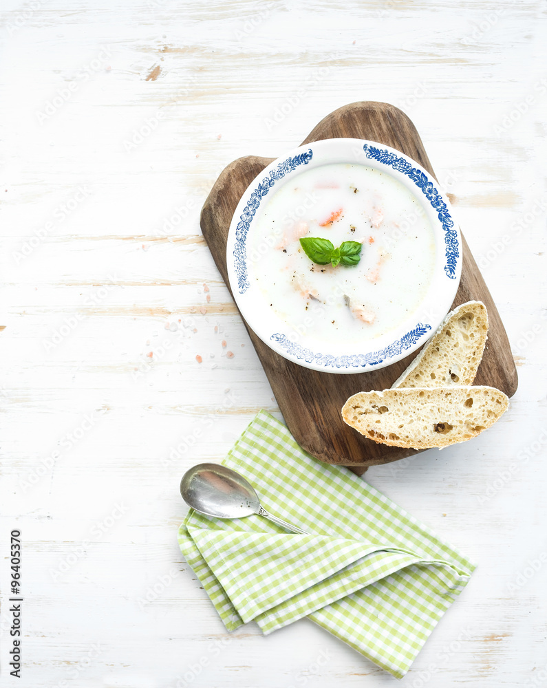 Scandinavian salmon soup with cream, fresh basil and bread in vintage ceramic plate on wooden servin