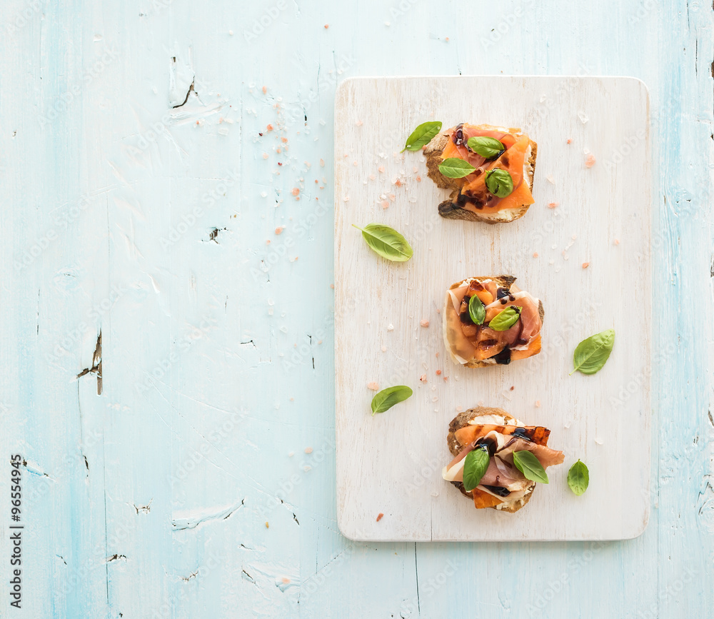 Bruschettas with Prosciutto，烤甜瓜，软奶酪和罗勒，放在木制服务板上，光线充足