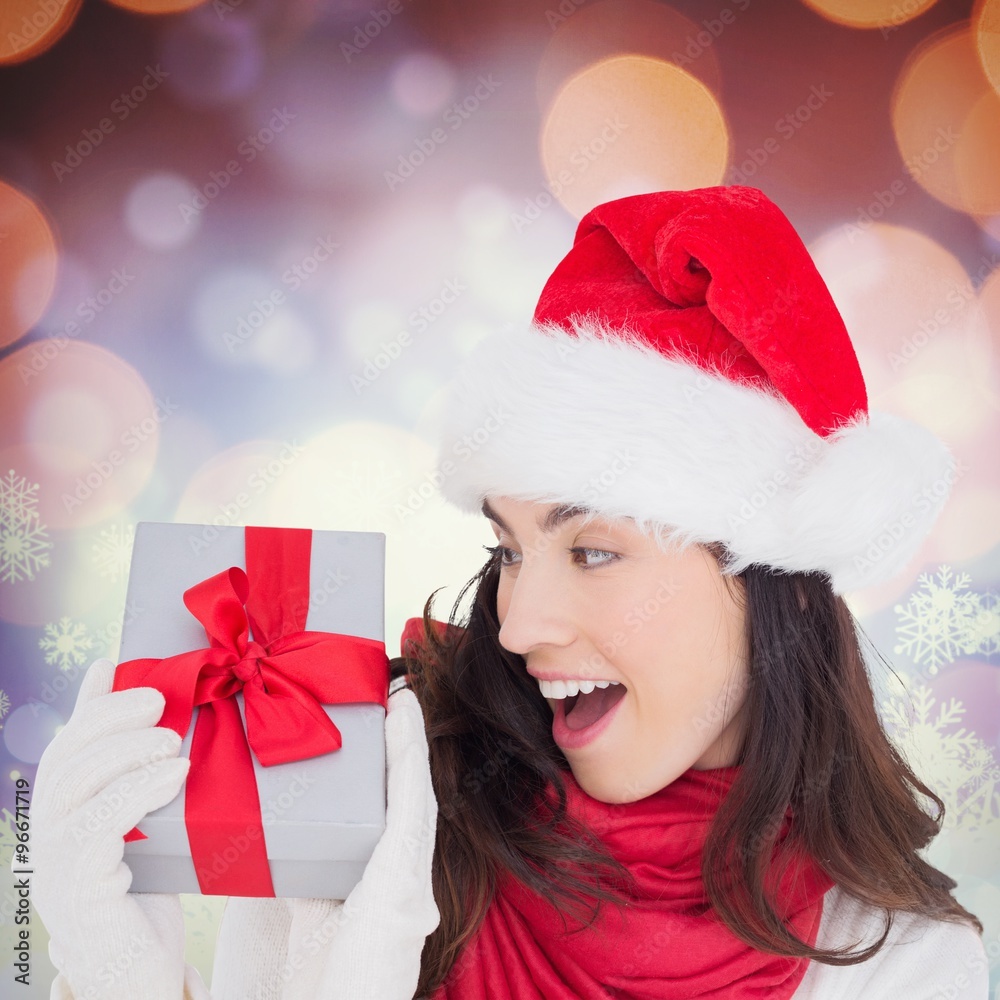 Composite image of astonished brunette in santa hat showing gift