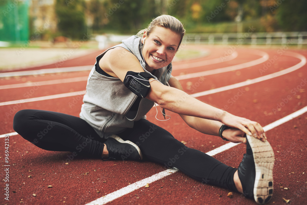 Athletic young woman stretching on track field