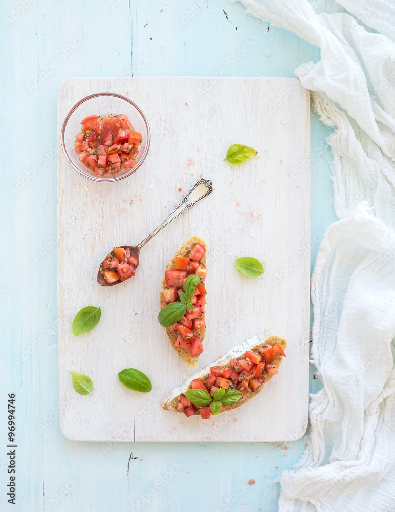 Tomato and basil bruschetta sandwich on white wooden serving board over rustic blue background, top 