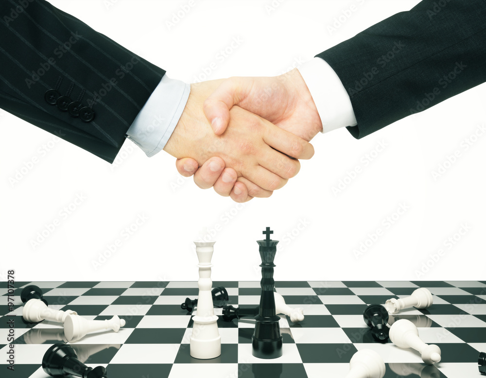 Businessmen shake hands above chess board