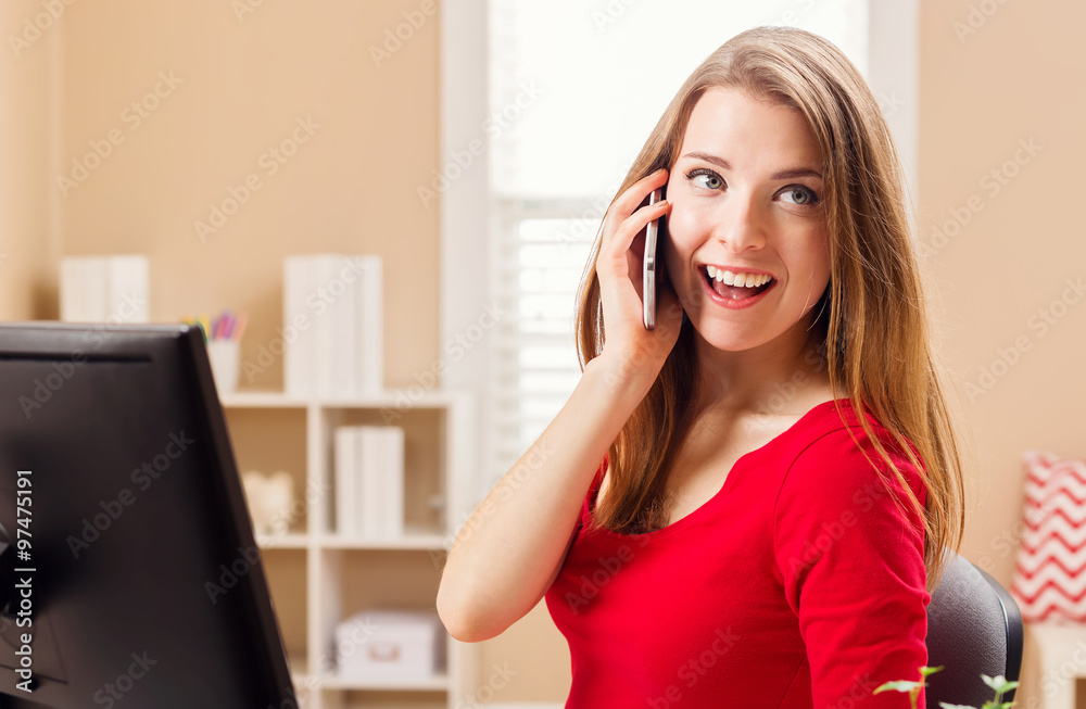 Happy young woman speaking on the phone in her office